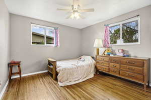 Bedroom with light wood-style floors, ceiling fan, and a textured wall