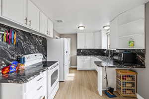 Kitchen featuring dark countertops, white appliances, decorative backsplash, white cabinetry, and light wood-style flooring