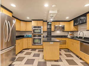 Kitchen featuring stainless steel appliances, a kitchen island, light wood finish cabinetry, recessed lighting, and dark stone counters