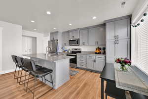 Kitchen featuring gray cabinets, a breakfast bar, stainless steel appliances, light stone countertops, and light wood-type flooring