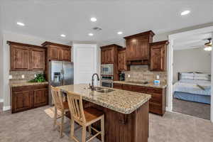 Kitchen with backsplash, a breakfast bar area, stainless steel appliances, a ceiling fan, and light stone countertops