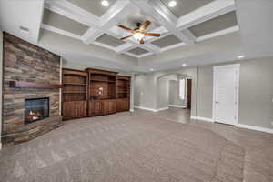 Unfurnished living room featuring arched walkways, ceiling fan, recessed lighting, coffered ceiling, and a stone fireplace