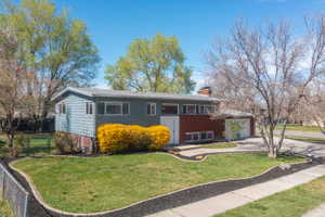 Split foyer home featuring driveway, a front yard, a chimney, and an attached garage