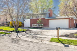 Split foyer home with driveway, brick siding, a garage, and a chimney