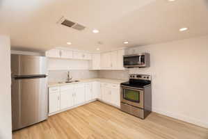 Kitchen with stainless steel appliances, white cabinets, light countertops, light wood finished floors, and recessed lighting