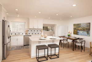 Kitchen with white cabinetry, a breakfast bar area, stainless steel appliances, backsplash, and light wood-style floors