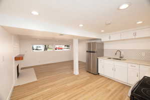 Kitchen featuring white cabinets, freestanding refrigerator, black electric range, decorative backsplash, and light wood finished floors