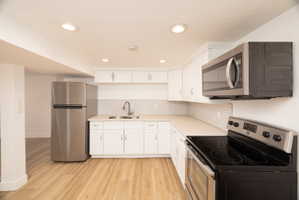 Kitchen with stainless steel appliances, white cabinets, light countertops, light wood finished floors, and decorative backsplash
