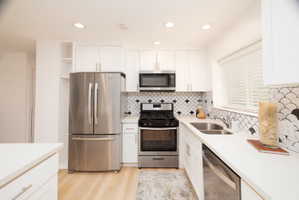 Kitchen with stainless steel appliances, white cabinets, light wood-style flooring, recessed lighting, and open shelves