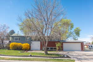 View of front of house with brick siding, a garage, driveway, and a front lawn