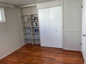 Unfurnished bedroom featuring dark wood finished floors, concrete block wall, and a closet