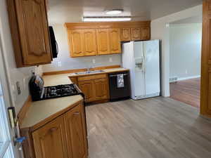 Kitchen with light countertops, light wood-style floors, gas range oven, black dishwasher, and crown molding