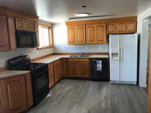 Kitchen featuring black appliances, wood finish cabinets, light countertops, and dark wood finished floors