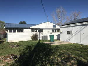 Rear view of house featuring a yard, solar panels, a patio area, and a metal roof
