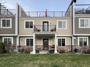Rear view of house with a balcony, stone siding, and a lawn