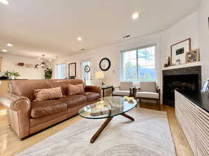 Living room with light wood-style flooring, suspended lighting, and a glass covered fireplace