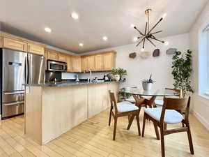 Kitchen featuring stainless steel appliances, a peninsula, dark stone countertops, light wood finish cabinets, and light wood finished floors