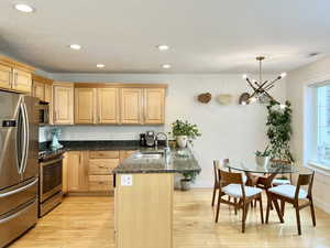 Kitchen with a peninsula, stainless steel appliances, dark stone countertops, a kitchen bar, and light wood-style flooring