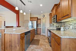 Kitchen featuring stainless steel appliances, wood finish cabinetry, vaulted ceiling, light stone countertops, and an island with sink