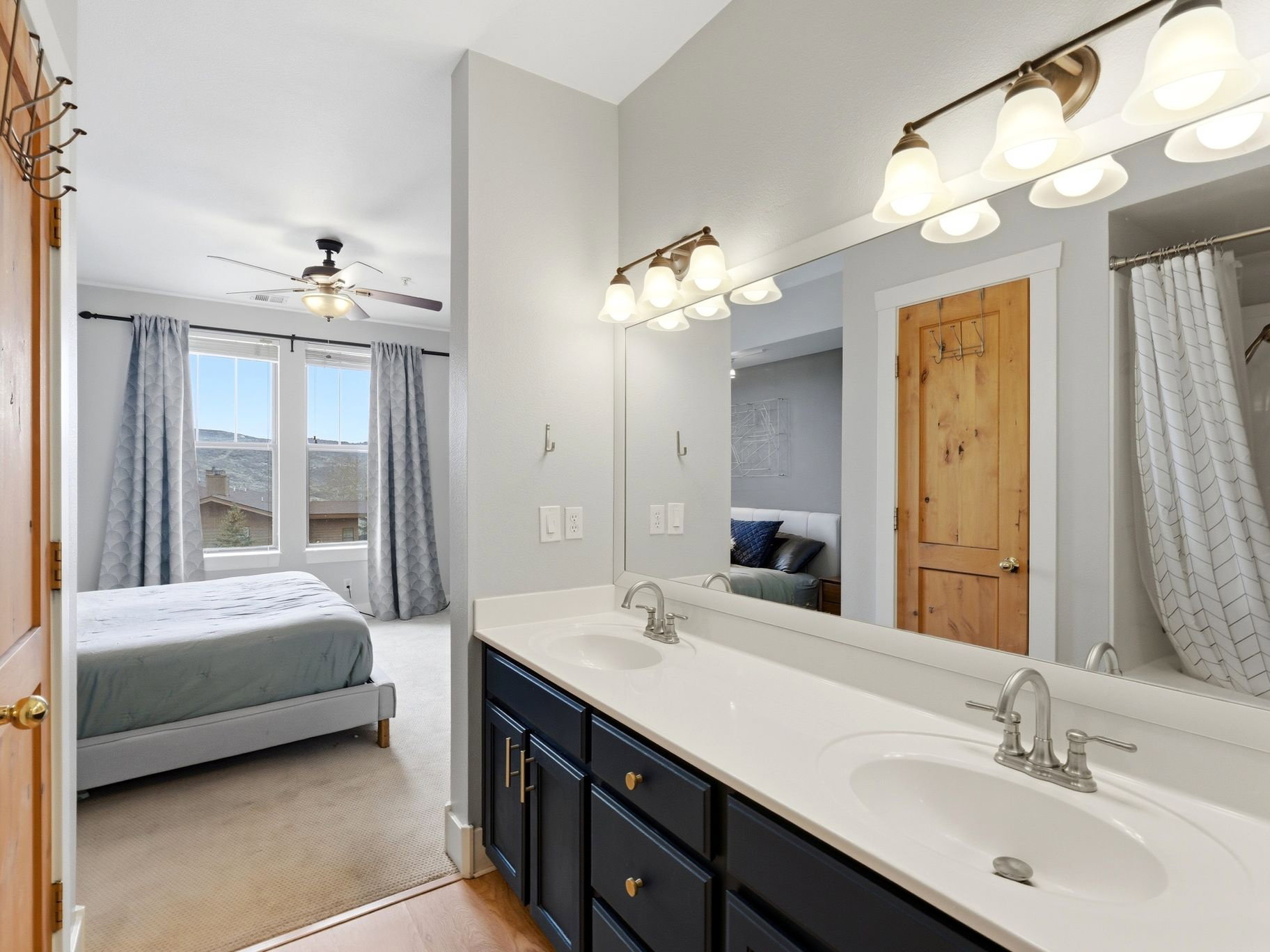 Ensuite bathroom with double vanity, curtained shower, light carpet, and ceiling fan