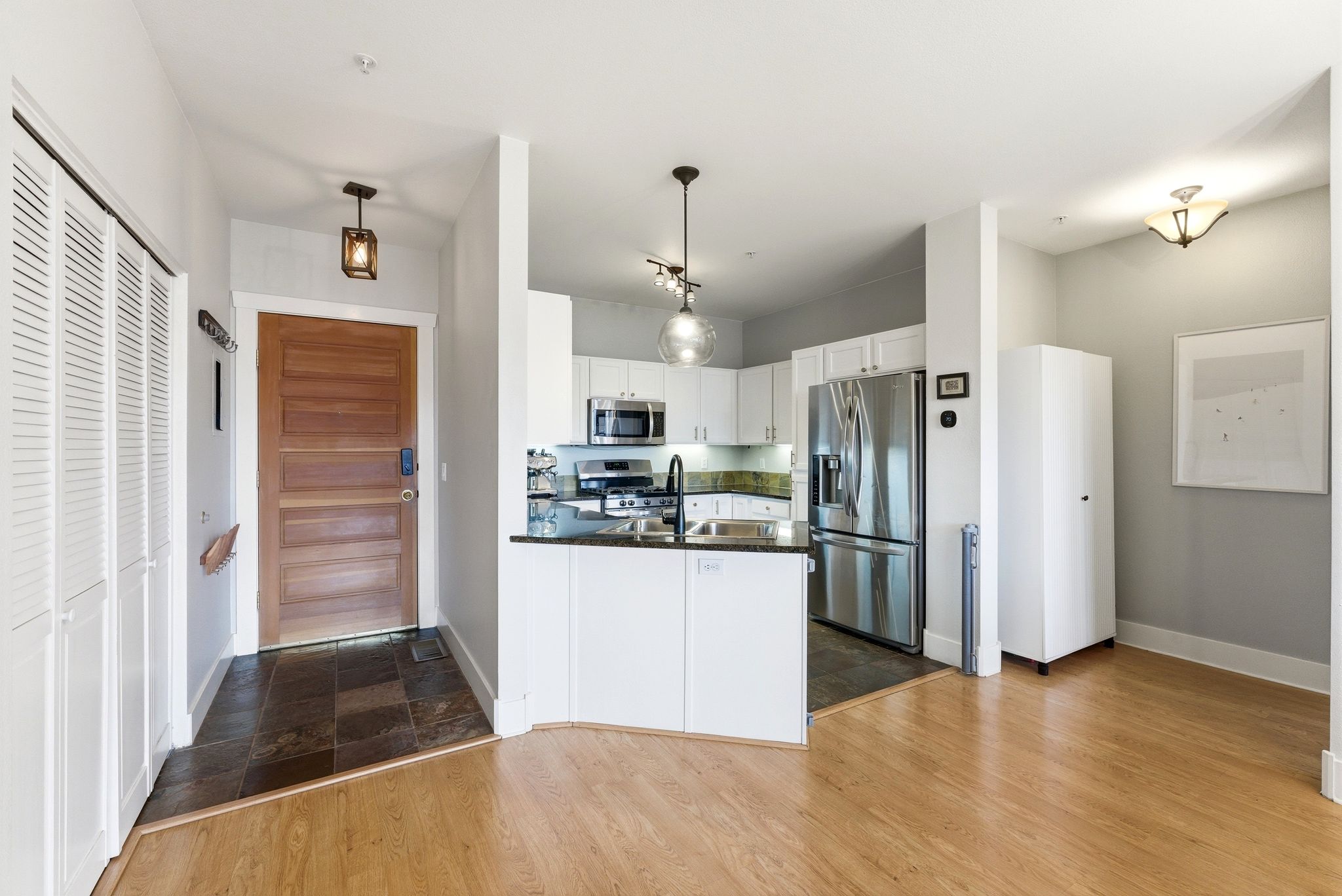 Kitchen with stainless steel appliances, hanging light fixtures, white cabinets, dark stone counters, and a peninsula