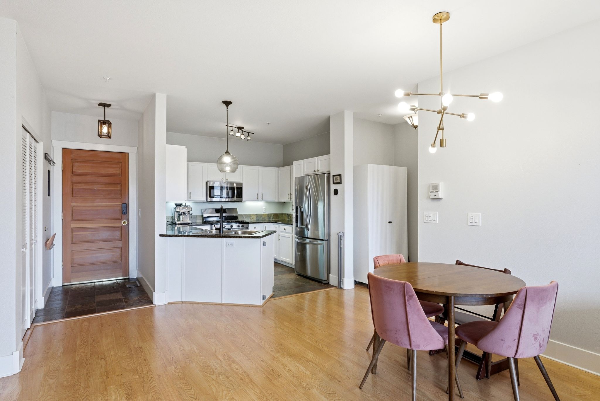 Kitchen featuring stainless steel appliances, dark wood-style flooring, white cabinetry, suspended lighting, and a peninsula