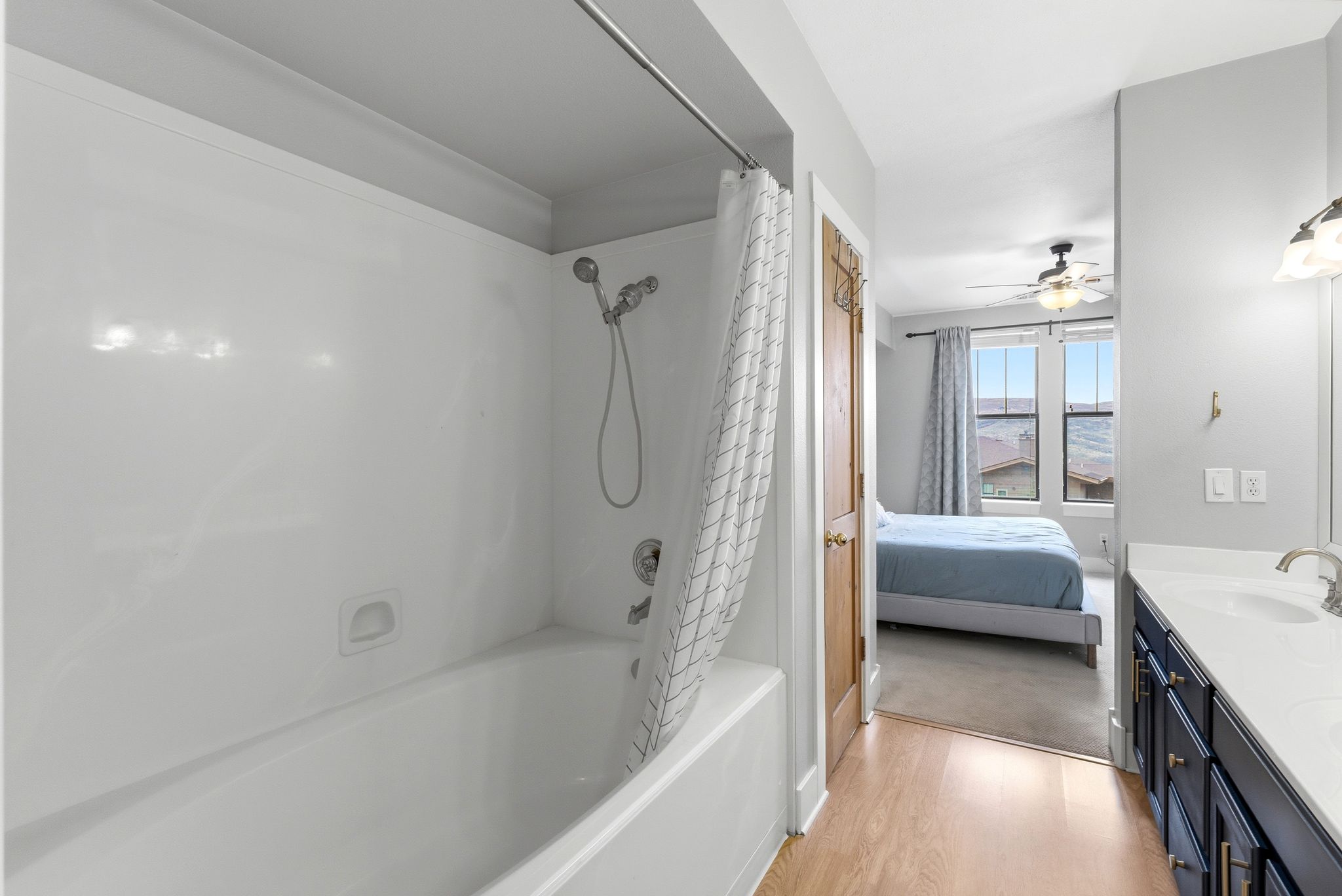 Ensuite bathroom featuring double vanity, shower / tub combo with curtain, light wood-type flooring, and a ceiling fan