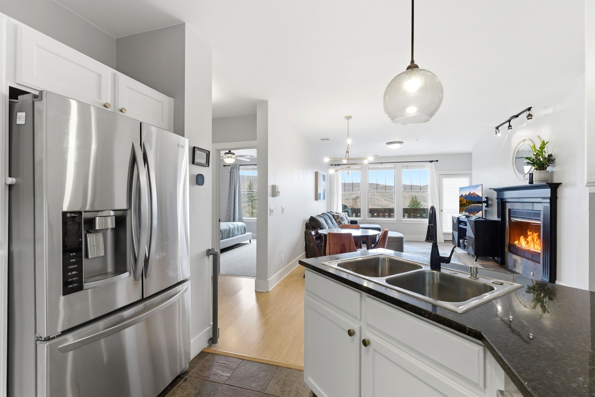 Kitchen featuring stainless steel refrigerator with ice dispenser, white cabinetry, open floor plan, hanging light fixtures, and a warm lit fireplace