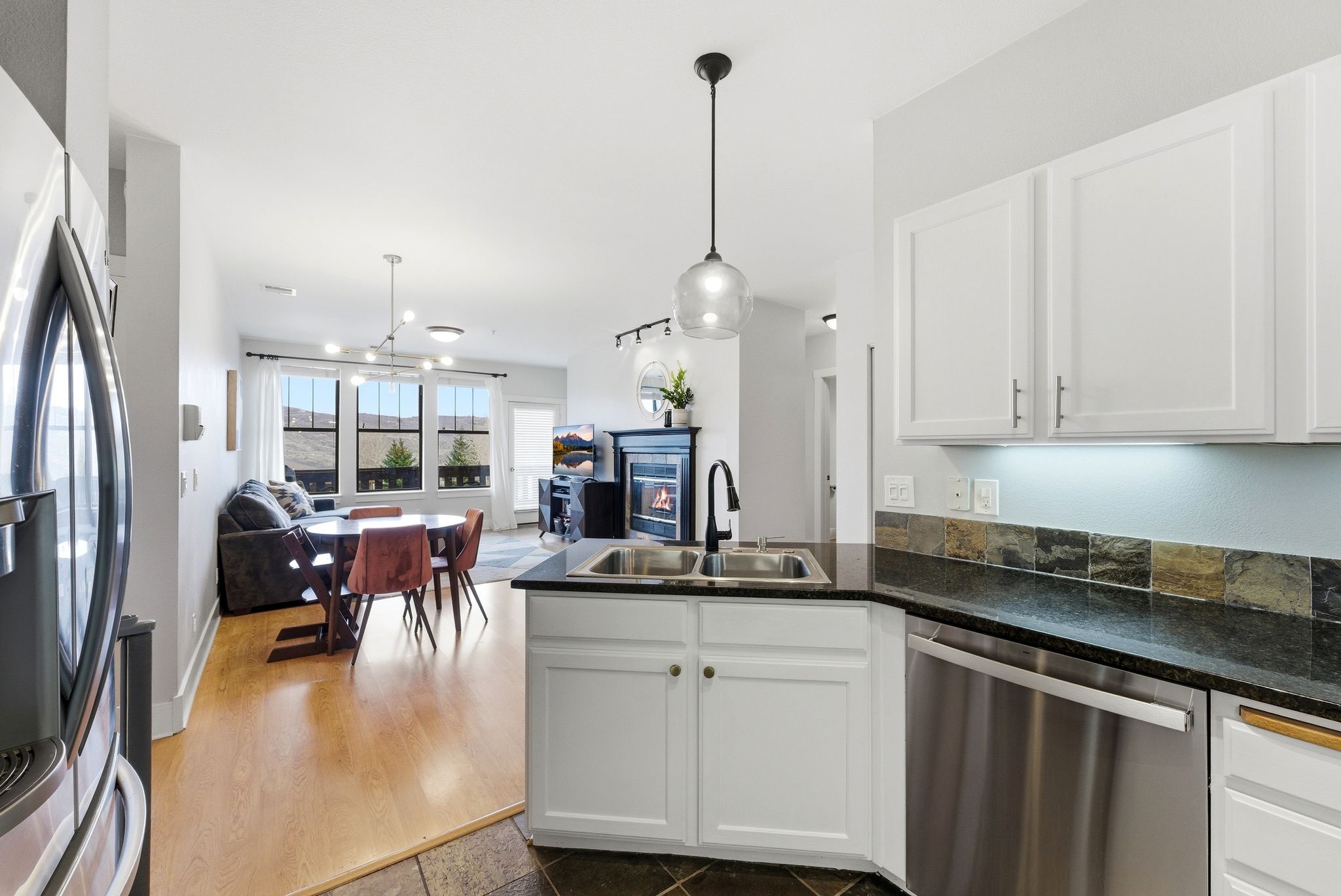 Kitchen featuring white cabinets, stainless steel appliances, a peninsula, open floor plan, and a glass covered fireplace
