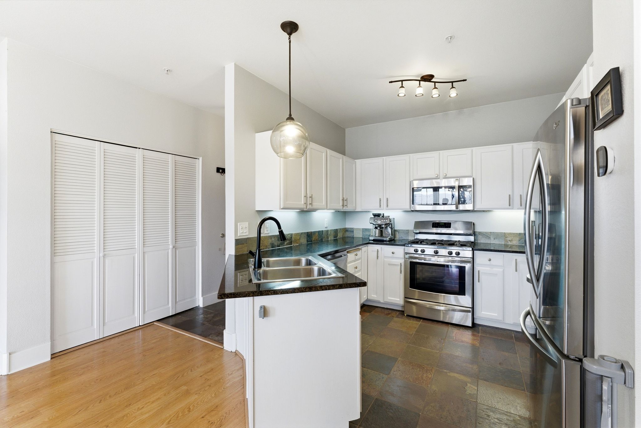 Kitchen with stainless steel appliances, white cabinetry, a peninsula, and hanging light fixtures