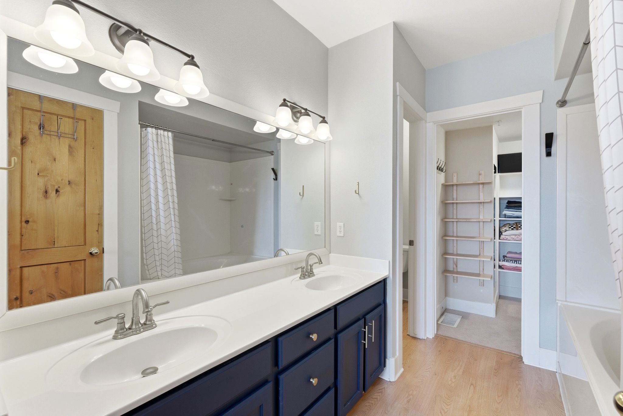 Full bathroom with double vanity, light wood-style flooring, a spacious closet, and shower / bath combination with curtain