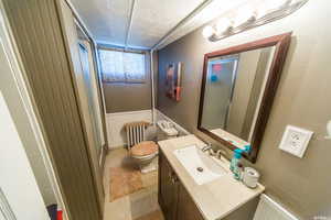Full bath featuring a textured ceiling, vanity, a shower with shower door, and a wainscoted wall