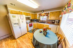 Kitchen featuring white appliances, light wood-style floors, a textured ceiling, tasteful backsplash, and dark countertops