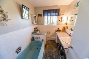 Bathroom with tile walls, vanity, a wainscoted wall, a bath, and dark stone finish floors