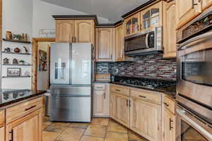 Kitchen with stainless steel appliances, glass insert cabinets, light wood finish cabinetry, and lofted ceiling