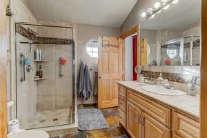 Bathroom with vanity, stone tile flooring, a shower stall, and tasteful backsplash