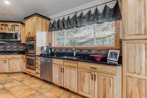 Kitchen with dark stone counters, light wood finish cabinetry, stainless steel appliances, glass fronted cabinets, and backsplash