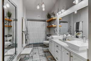 Full bathroom featuring double vanity, light stone finish flooring, and a shower with shower curtain