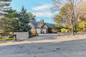 View of front of home featuring driveway, a chimney, and a shingled roof