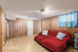 Living room with light wood-style flooring, a textured ceiling, and wood walls