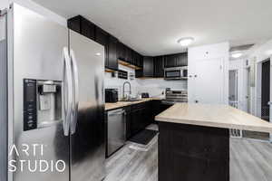 Kitchen with stainless steel appliances, a center island, wooden counters, light wood finished floors, and dark cabinetry
