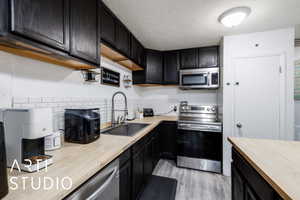 Kitchen with dark cabinets, stainless steel appliances, butcher block counters, light wood-style flooring, and decorative backsplash