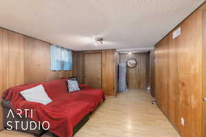 Sitting room featuring light wood-type flooring, wooden walls, and a textured ceiling
