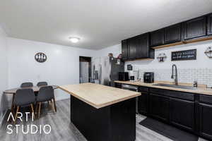 Kitchen featuring dark cabinets, a center island, stainless steel appliances, and light wood finished floors