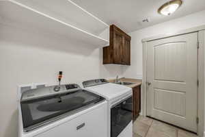 Laundry room featuring washer and clothes dryer, light tile patterned flooring, cabinet space, and a textured ceiling
