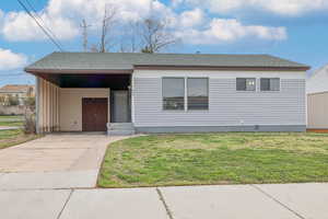 View of front of home featuring an attached carport, roof with shingles, concrete driveway, a front yard, and covered porch