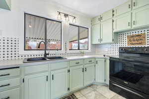 Kitchen featuring green cabinetry, black electric range, decorative backsplash, light countertops, and a textured ceiling