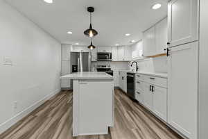 Kitchen featuring white cabinetry, a center island, stainless steel appliances, light wood-style flooring, and pendant lighting