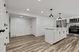 Kitchen with stainless steel appliances, a kitchen island, white cabinets, light wood-type flooring, and pendant lighting