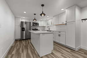 Kitchen with stainless steel appliances, white cabinets, light wood-style flooring, and a kitchen island